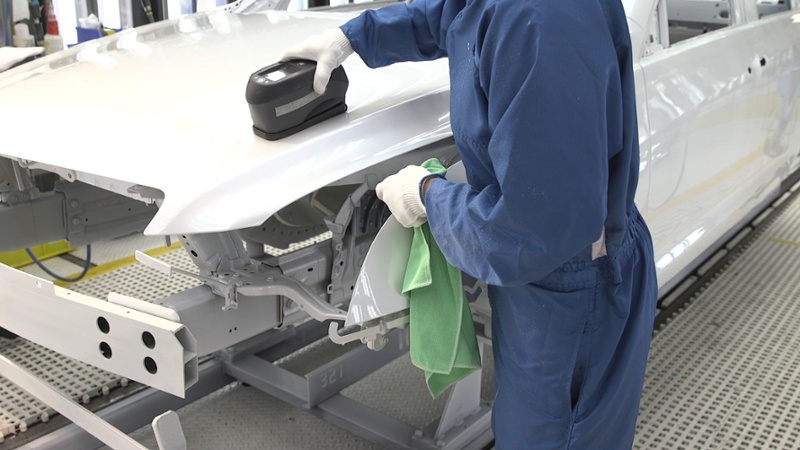 mechanic in blue overalls cleaning hood of car